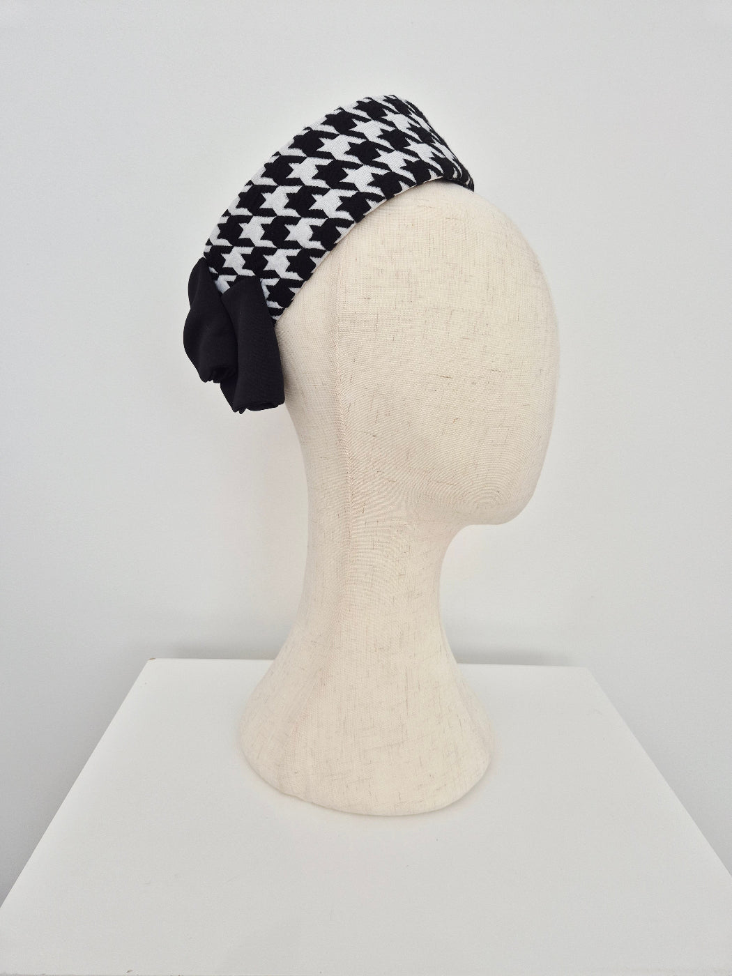 Black and white houndstooth pattern pillbox headpiece on a mannequin head against a white background