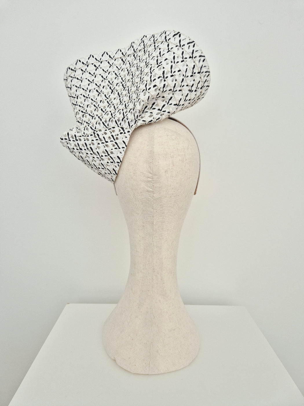 black and white straw headpiece on a mannequin against a plain background back view