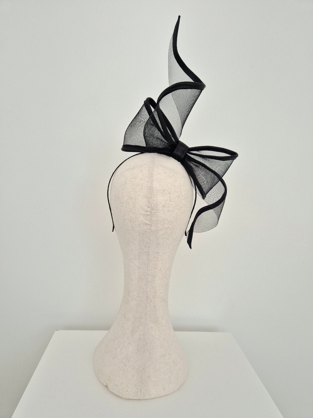 Black bow fascinator on a mannequin head against a white background back view