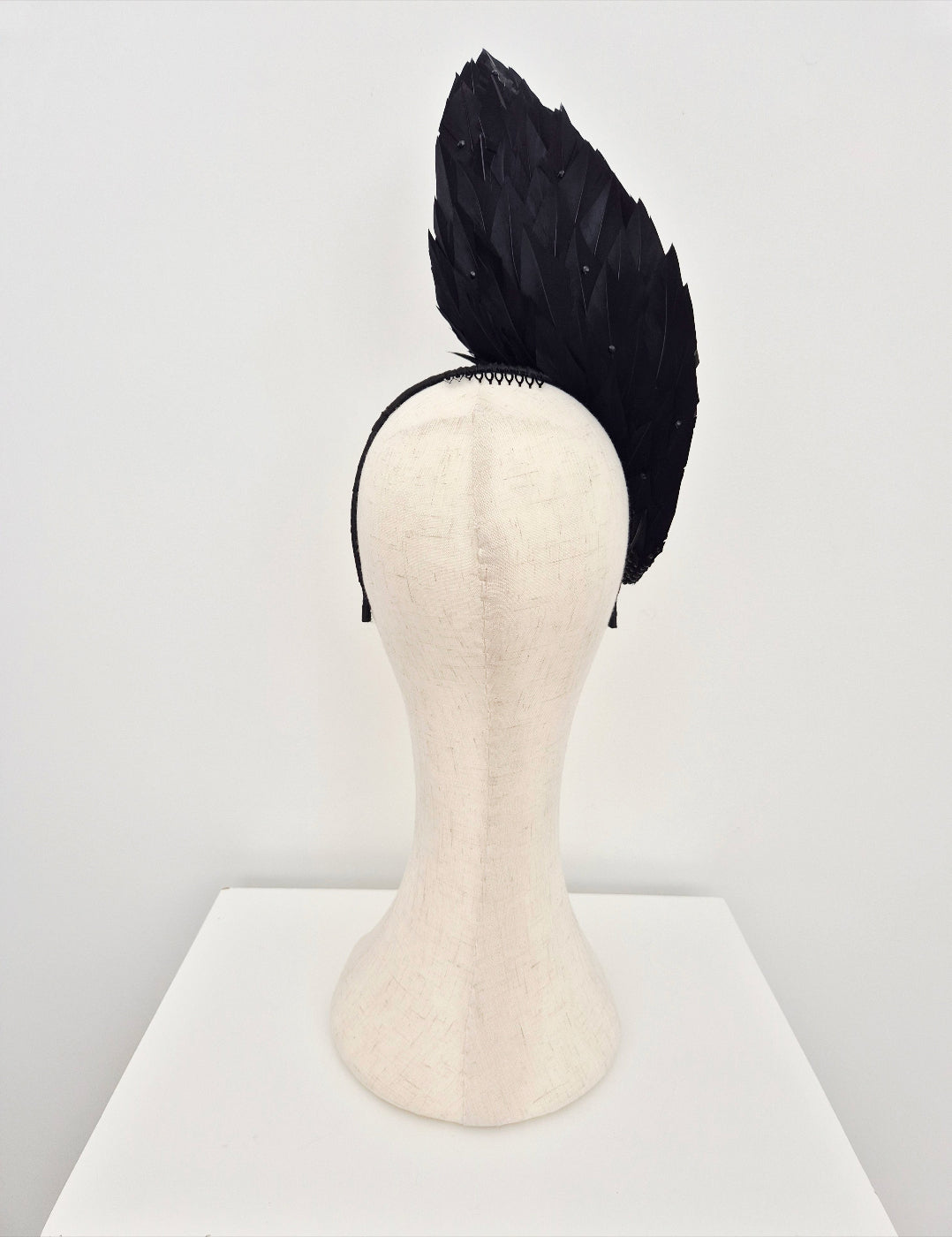 Black feathered headpiece on a mannequin head against a white background