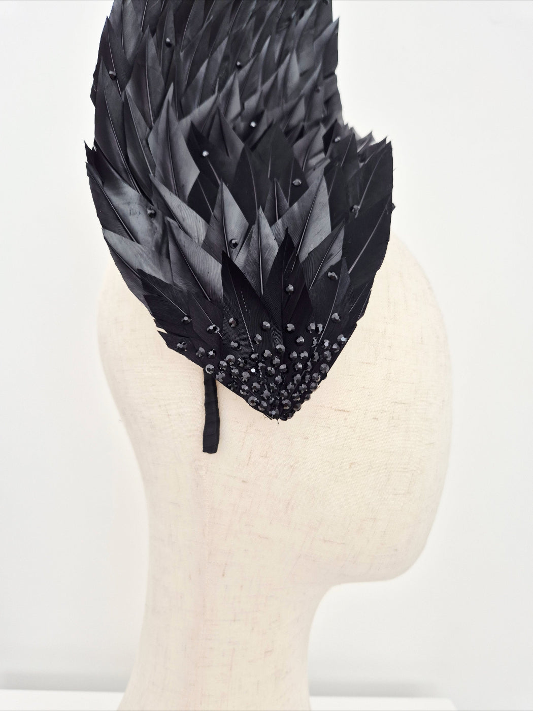 Black feathered headpiece on a mannequin head against a white background close up