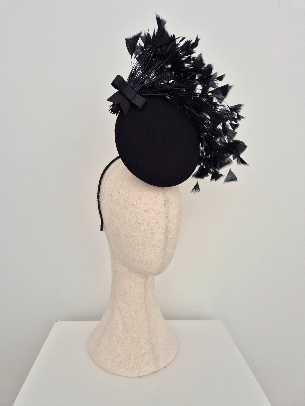 Black feathered headpiece on a mannequin head against a white background side view