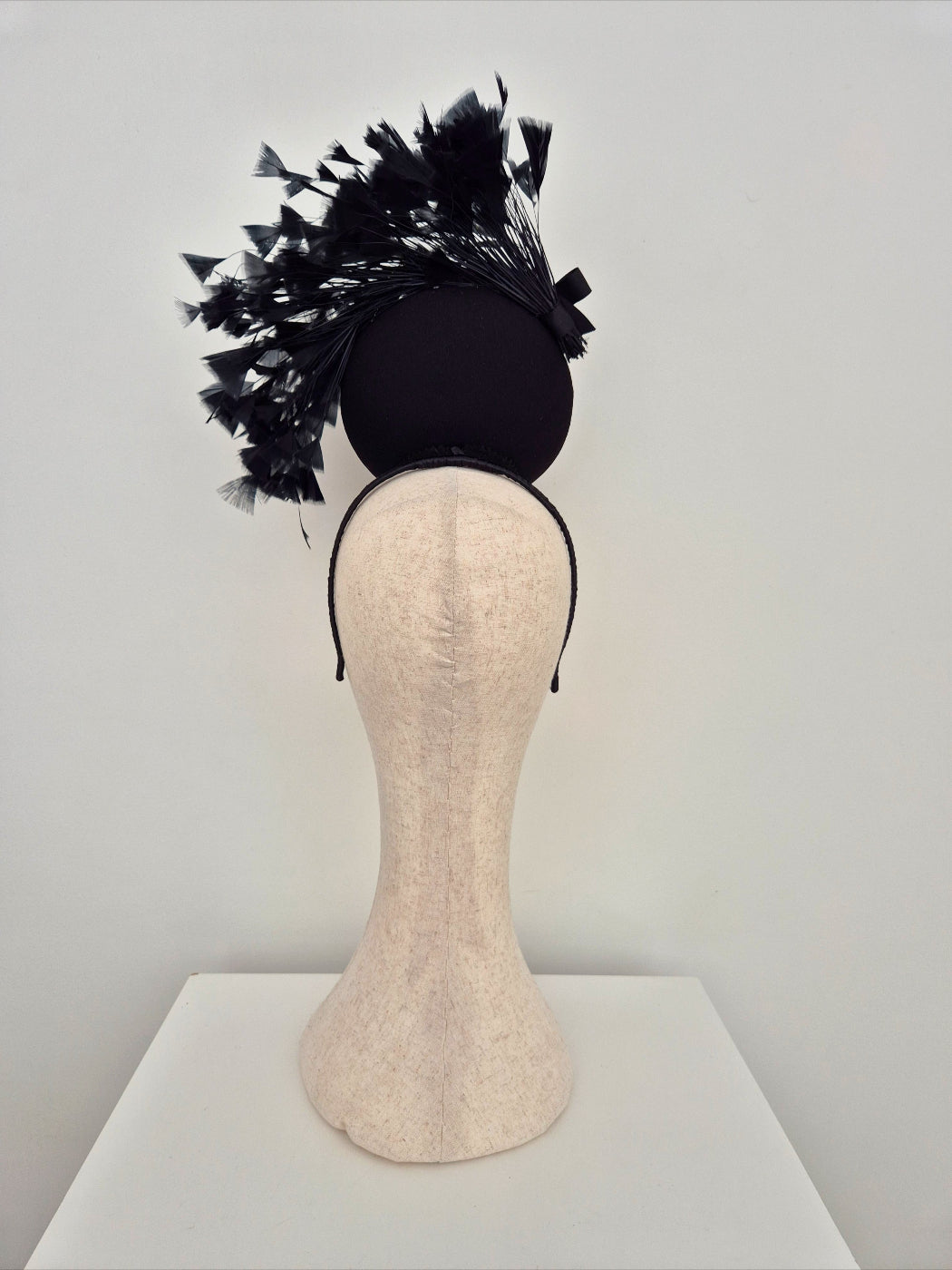 Black feathered headband on a mannequin head against a plain background back view