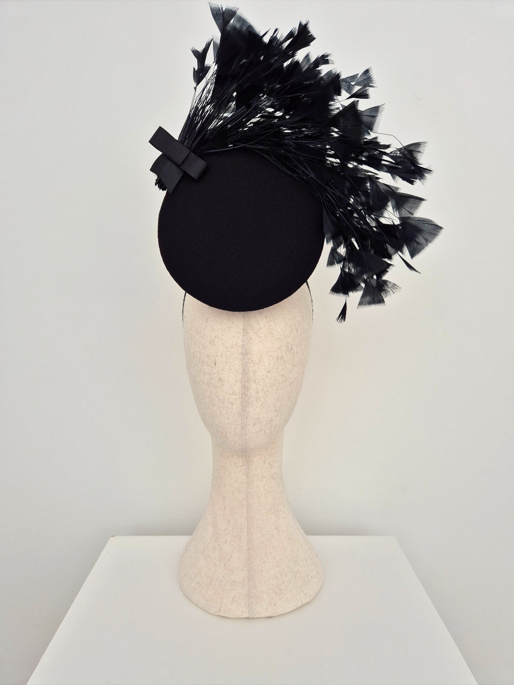 Black feathered percher headpiece on a mannequin head against a white background