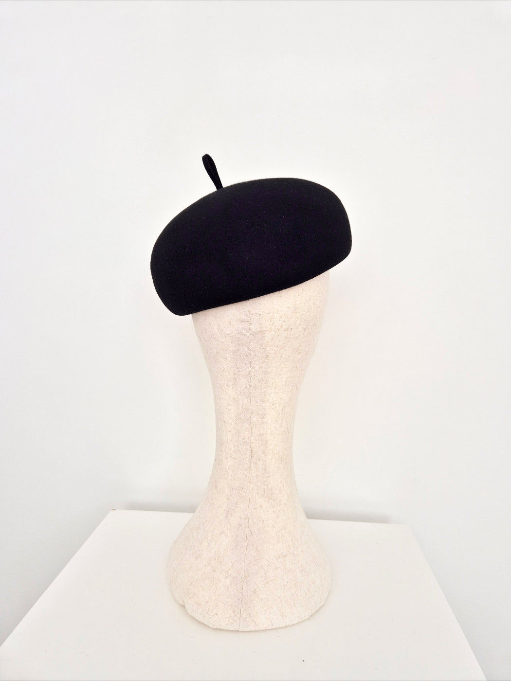 A black felt beret displayed on a mannequin head against a plain white background. back view