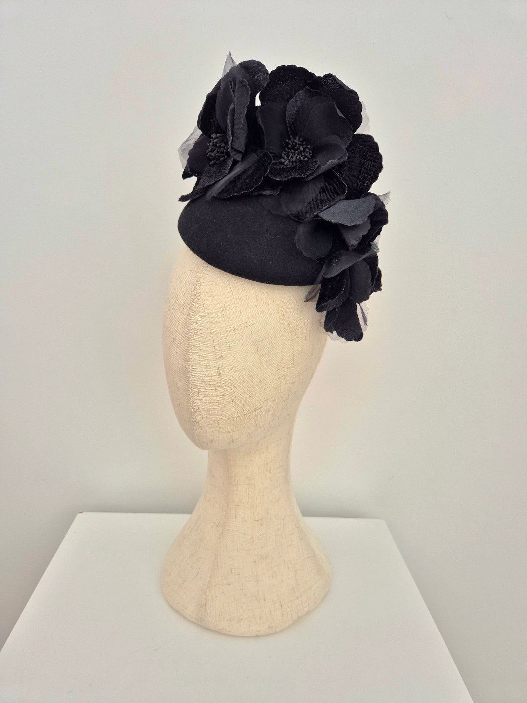 Black fascinator with floral details on a mannequin head against a white background side view