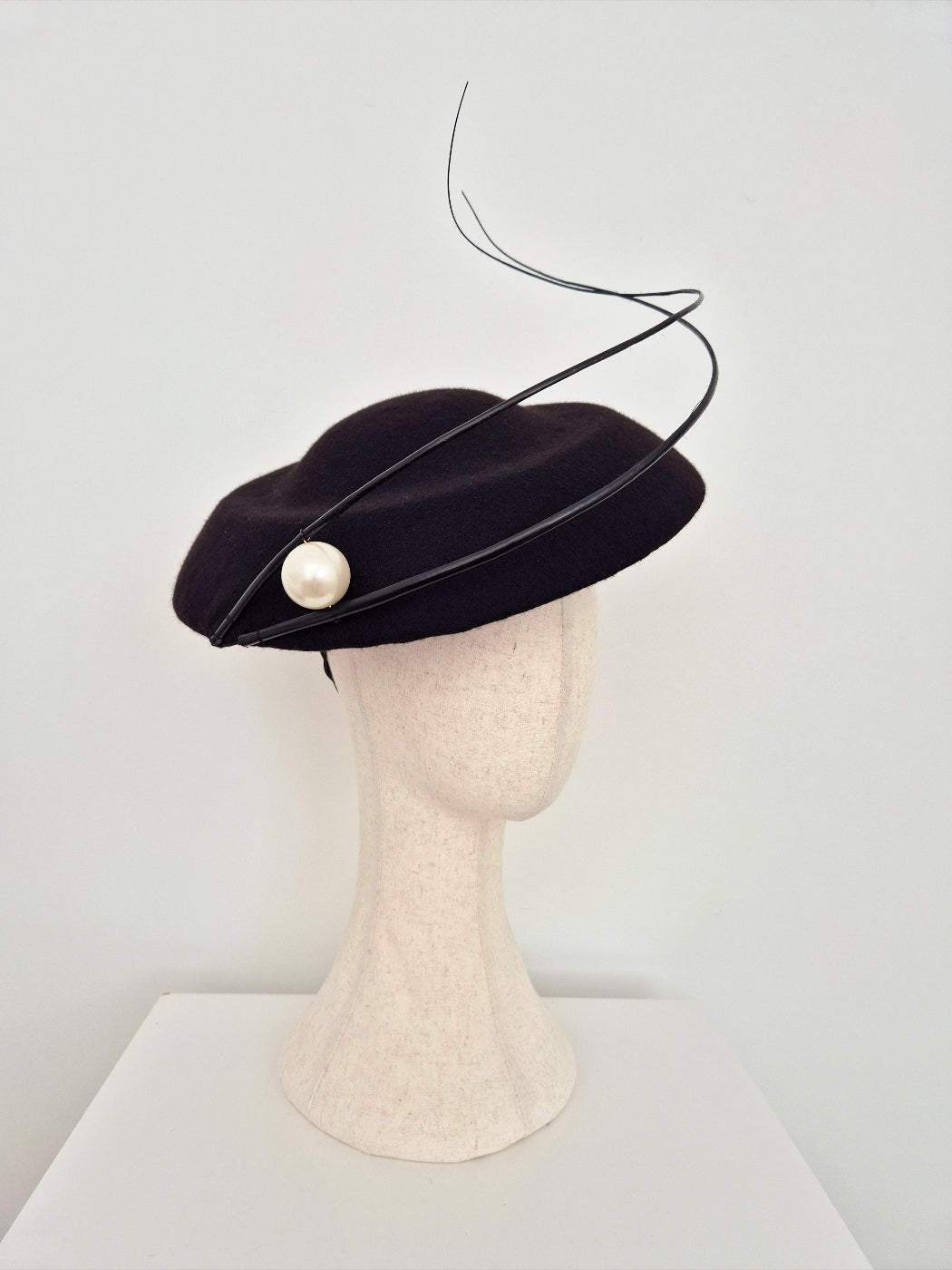 Black felt  hat with a pearl on a mannequin head against a white background side view
