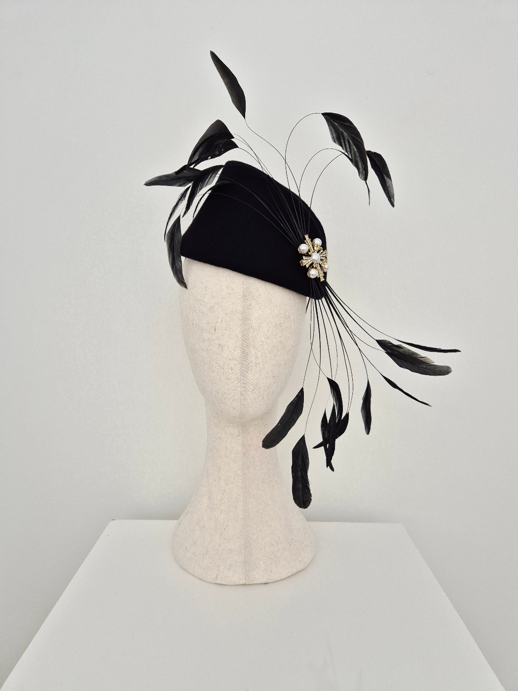 Black headband with feather accents on a mannequin head against a light gray background
