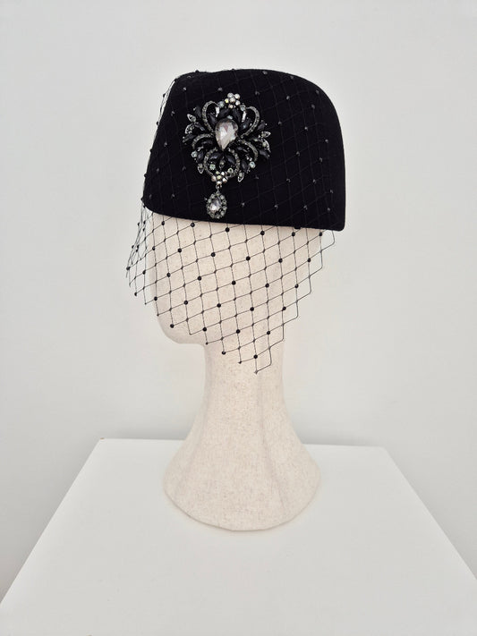 Black headpiece with on a white background with a brooch and rhinestone veiling side view