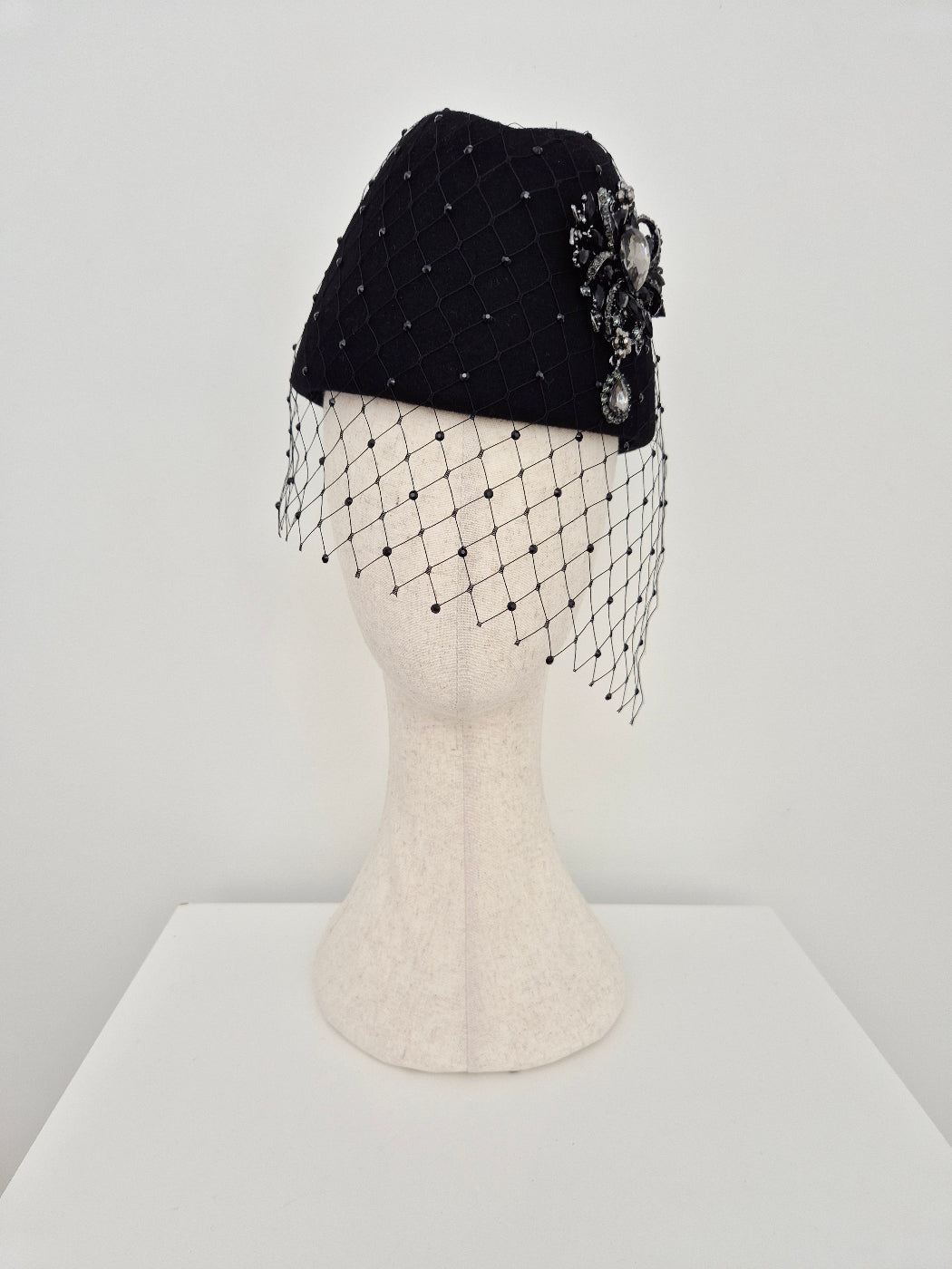 Black headpiece with decorative brooch and a rhinestone veil on a mannequin head against a white background