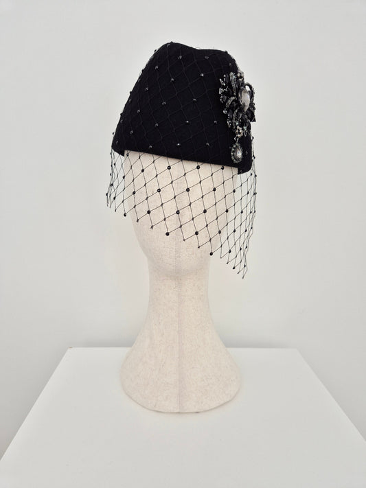 Black headpiece with decorative brooch and a rhinestone veil on a mannequin head against a white background