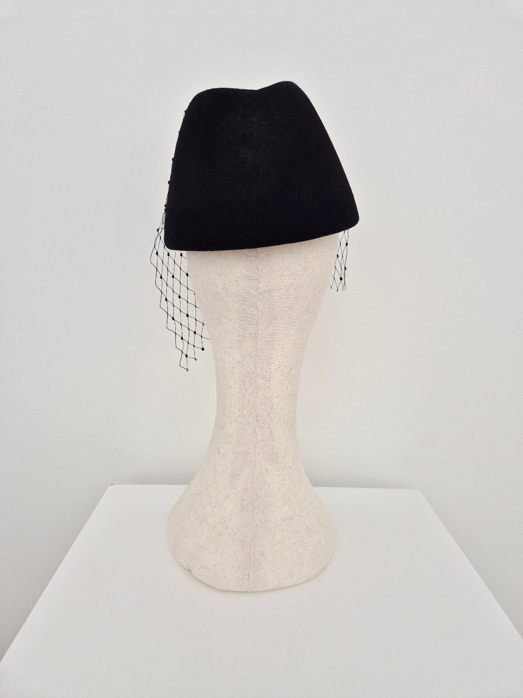 Black topper headpiece with veiling and brooch back view on a manniquin head against a white background