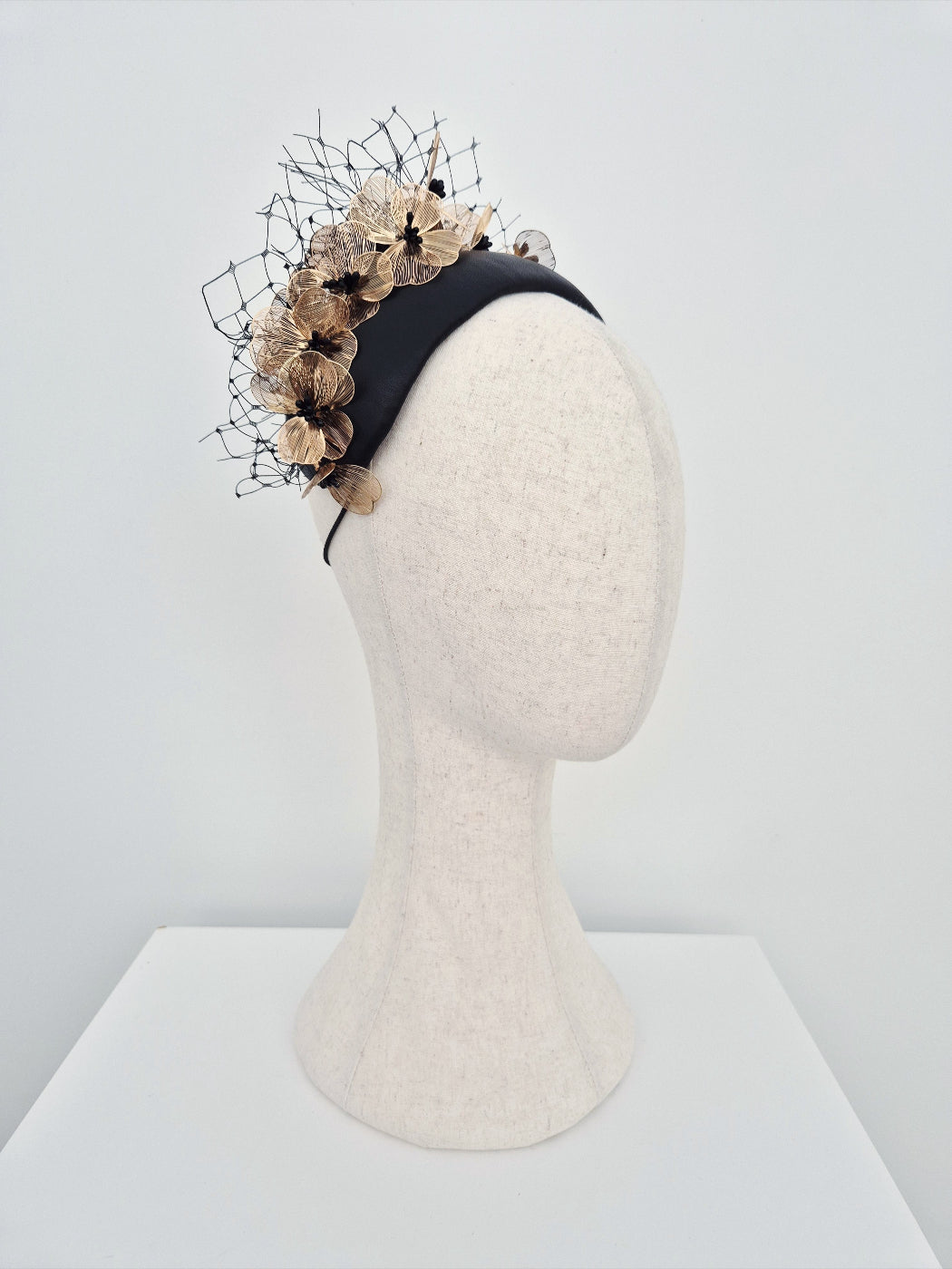 Black bandeau headpiece with decorative floral and metallic accents on a mannequin head against a white background side view