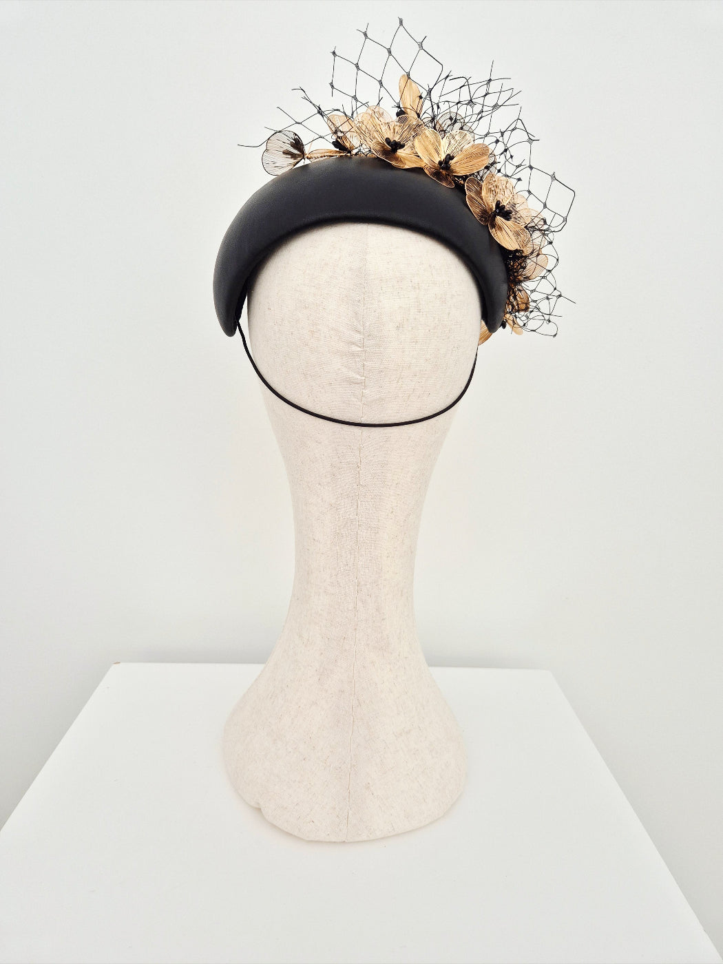 Black bandeau headpiece with decorative floral and netting on a mannequin head against a white background back view
