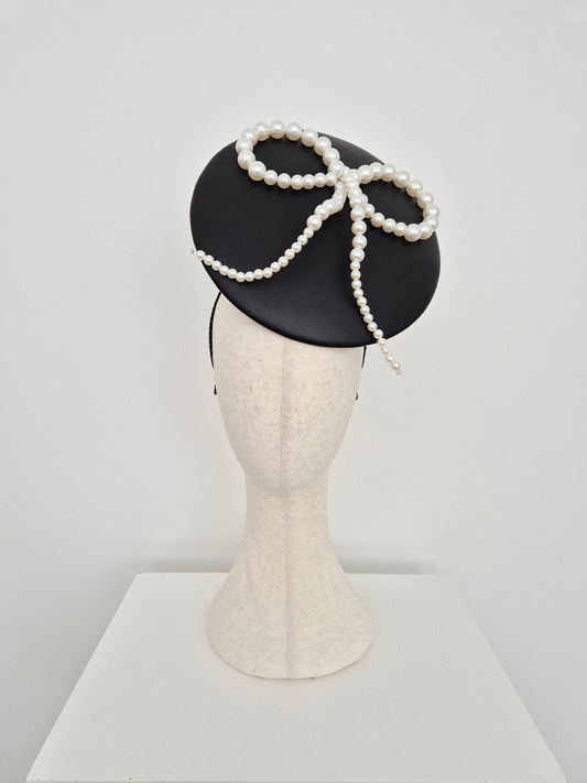 Black leather percher headpiece with white pearl bow on a manniquin head on a white background side front