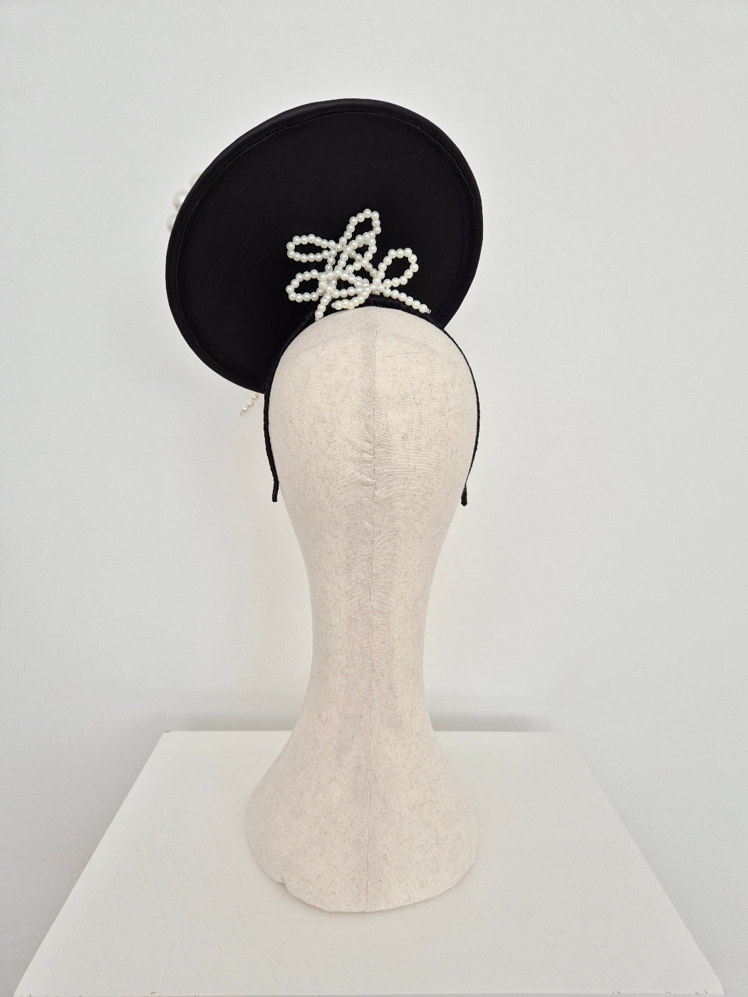 Black leather plate headpiece with  pearl bows on a manniquin head against  a white background back view