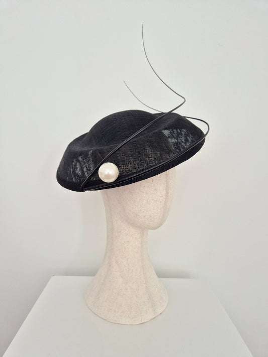 A black straw fascinator hat with a single white pearl accent, and 2 thin black quills, displayed on a beige mannequin head against a white background.side view