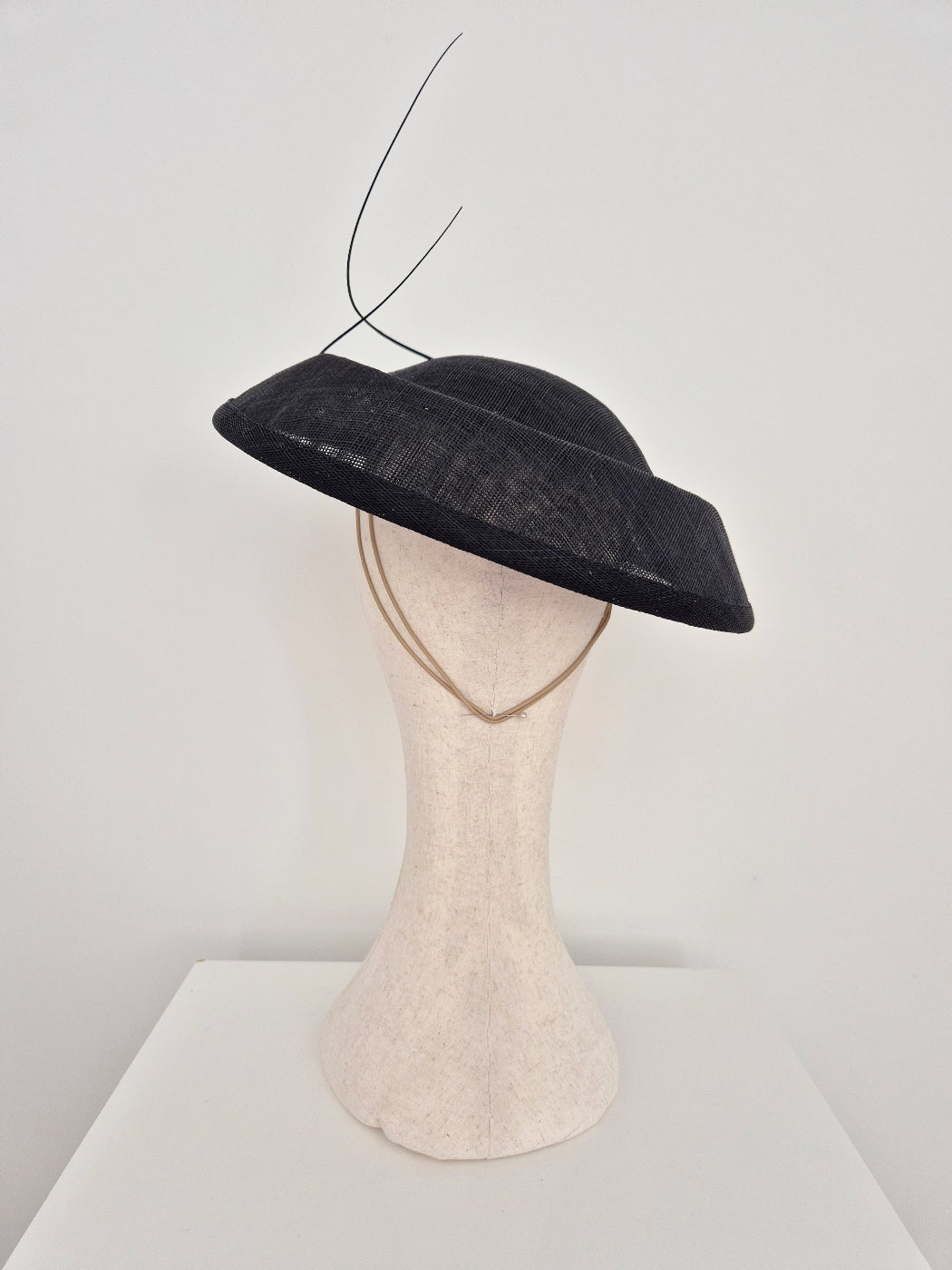 A black straw wide-brimmed fascinator hat with 2 quills displayed on a cream-colored mannequin head against a plain white background.back view