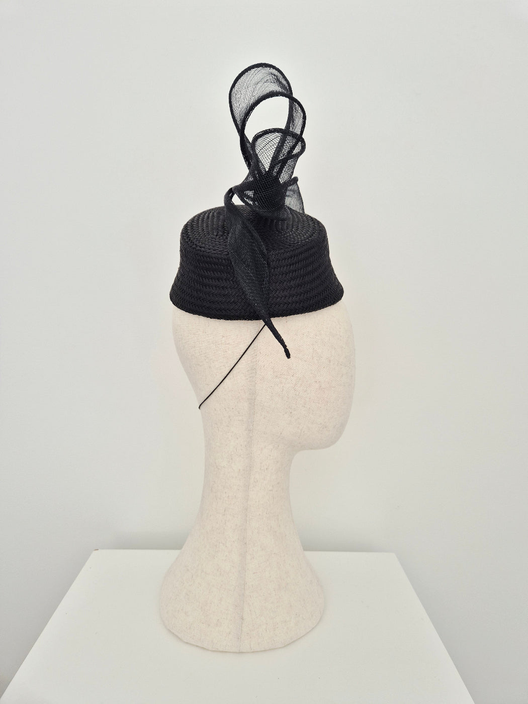 black straw headpiece with bow on a maniquin head against a white wall side view