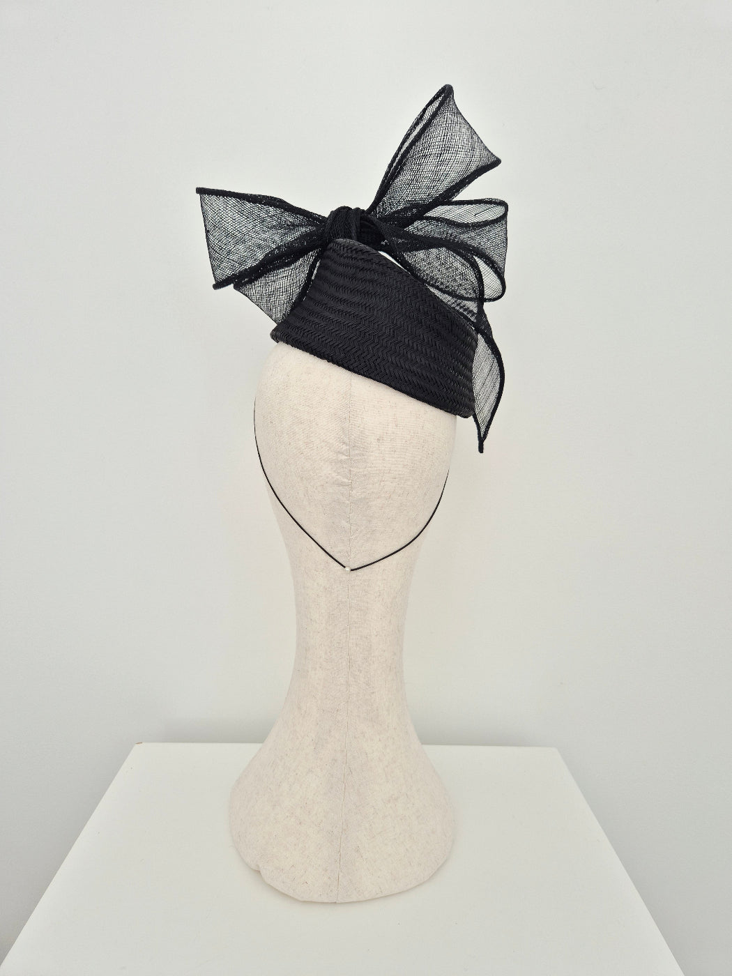 black straw headpiece with bow on a manniquin head against a white background back view