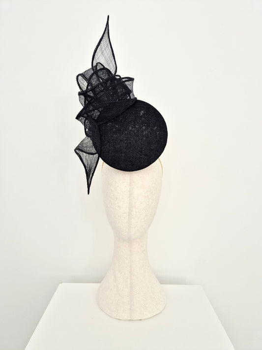 A black fascinator percher with a knotted tail detail, displayed on a cream-colored mannequin head against a plain white background.