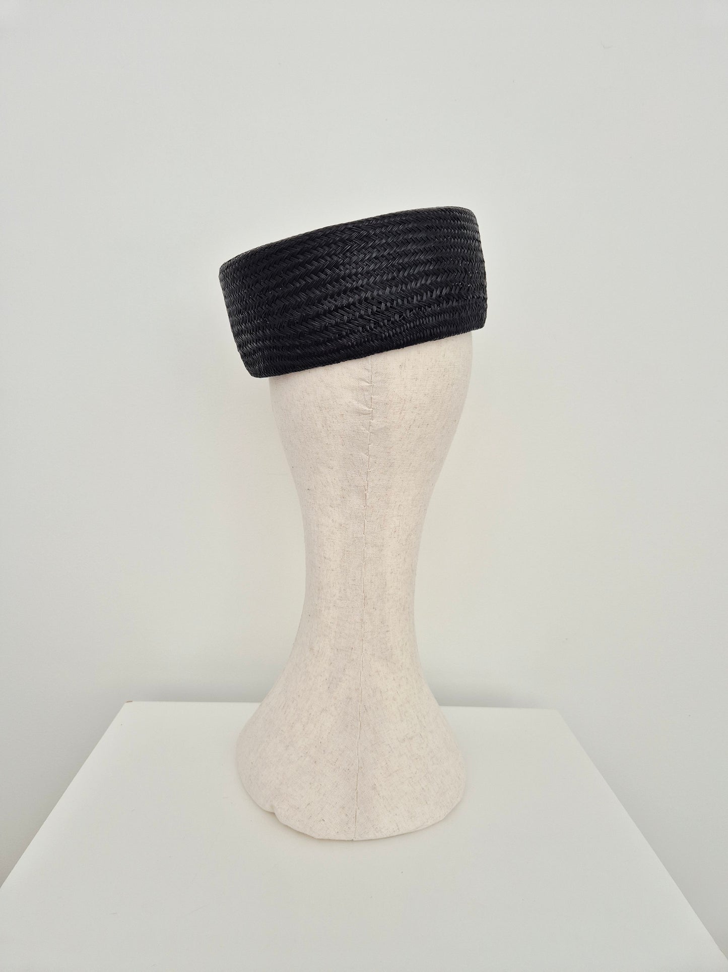 A black woven straw hat displayed on a cream-colored mannequin head stand against a plain white background.back view
