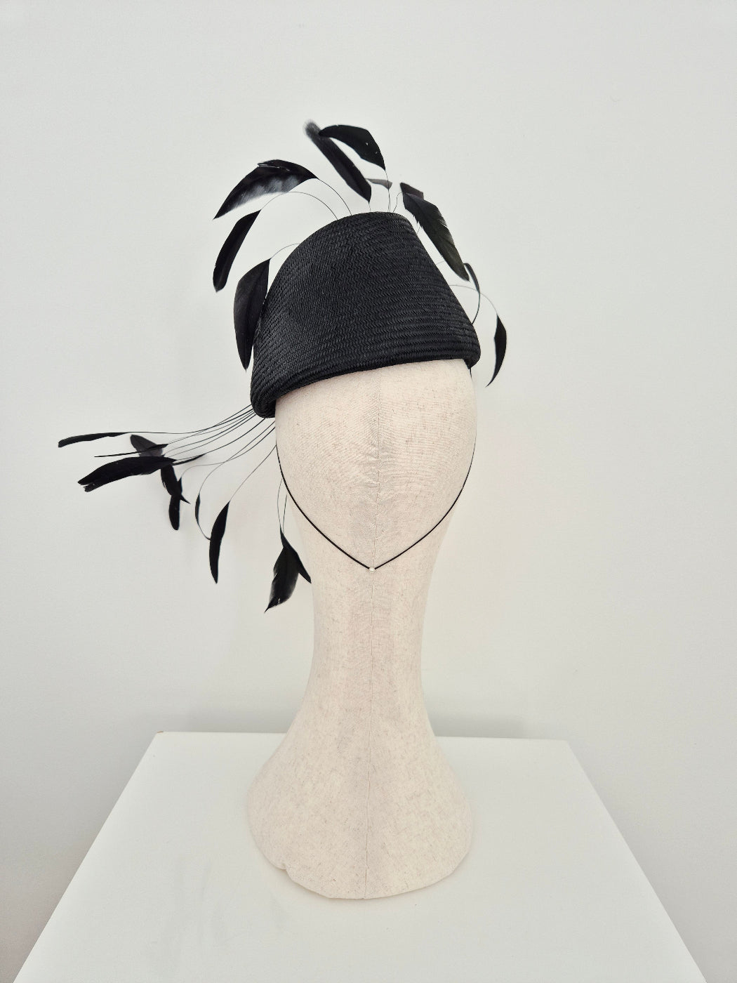 A black fascinator hat with long black feather accents, displayed on a cream-colored mannequin head against a plain white background. back view
