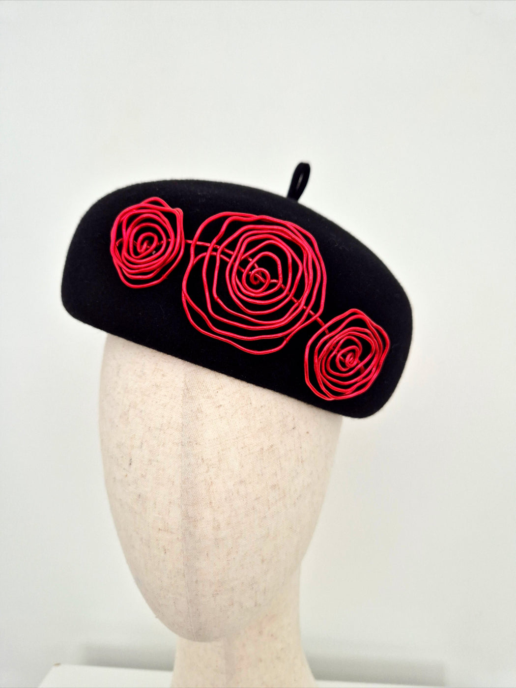 A black felt beret with red wire roses, on a mannequin head against a plain white background close up