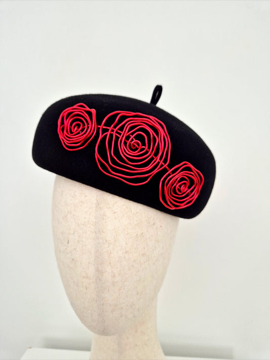 A black felt beret with red wire roses, on a mannequin head against a plain white background close up