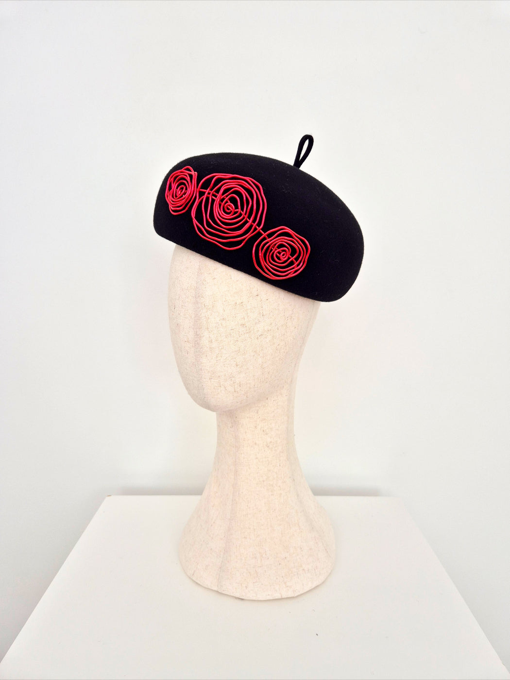 A black felt beret with red wire roses, on a mannequin head against a white background side view