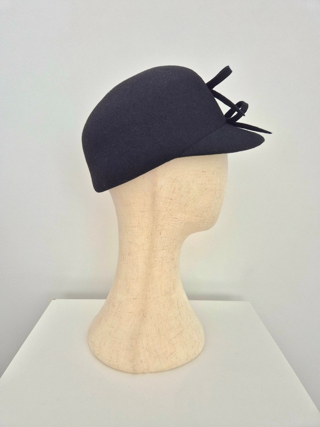 Black hat with bows on a mannequin head against a white background side view
