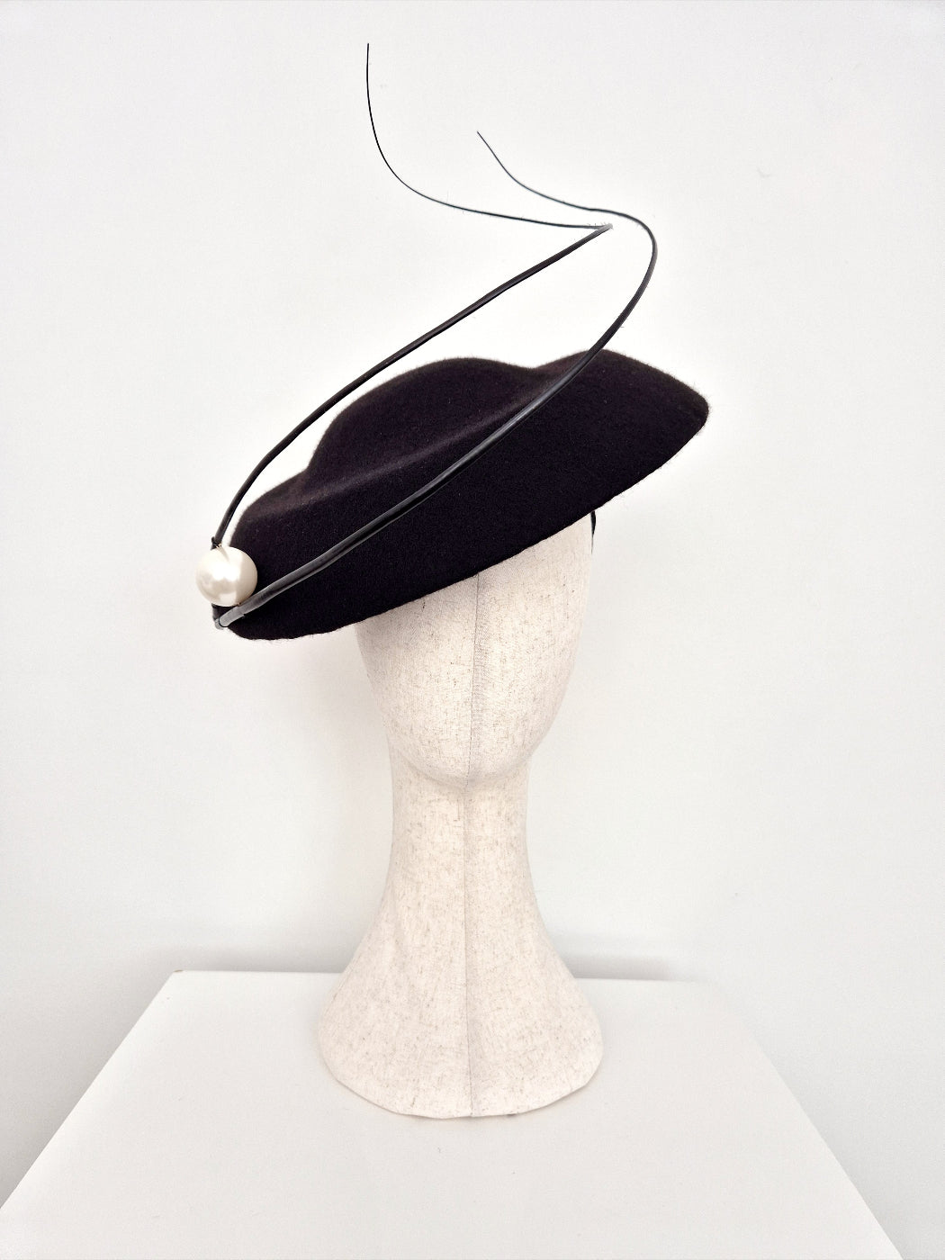 Black hat with a pearl on a mannequin head against a white background