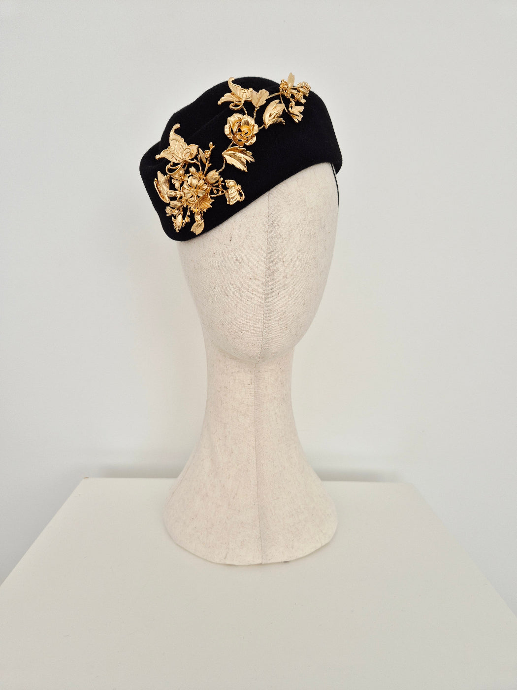 Black headpiece wool felt with gold floral designs on a mannequin head against a white background