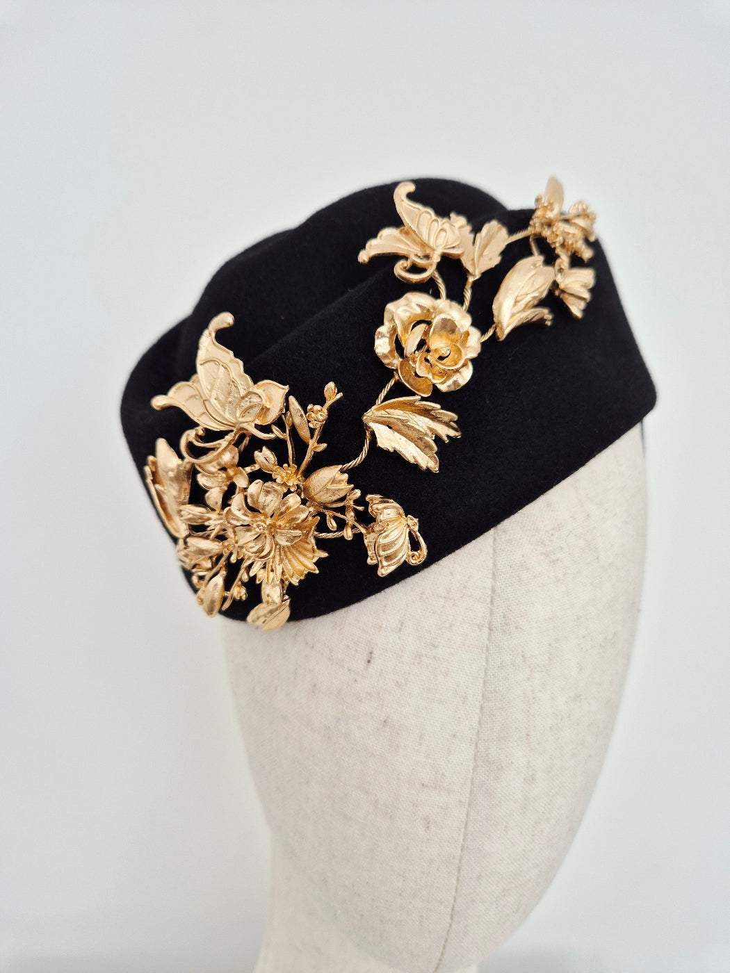 Black headpiece wool felt hostess style with gold floral embellishments on a white background  close up