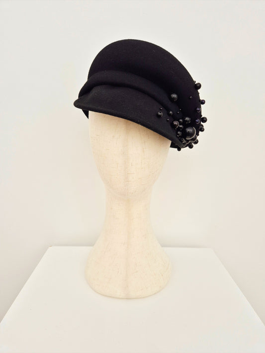 Black hat with bead embellishments on a mannequin head against a white background