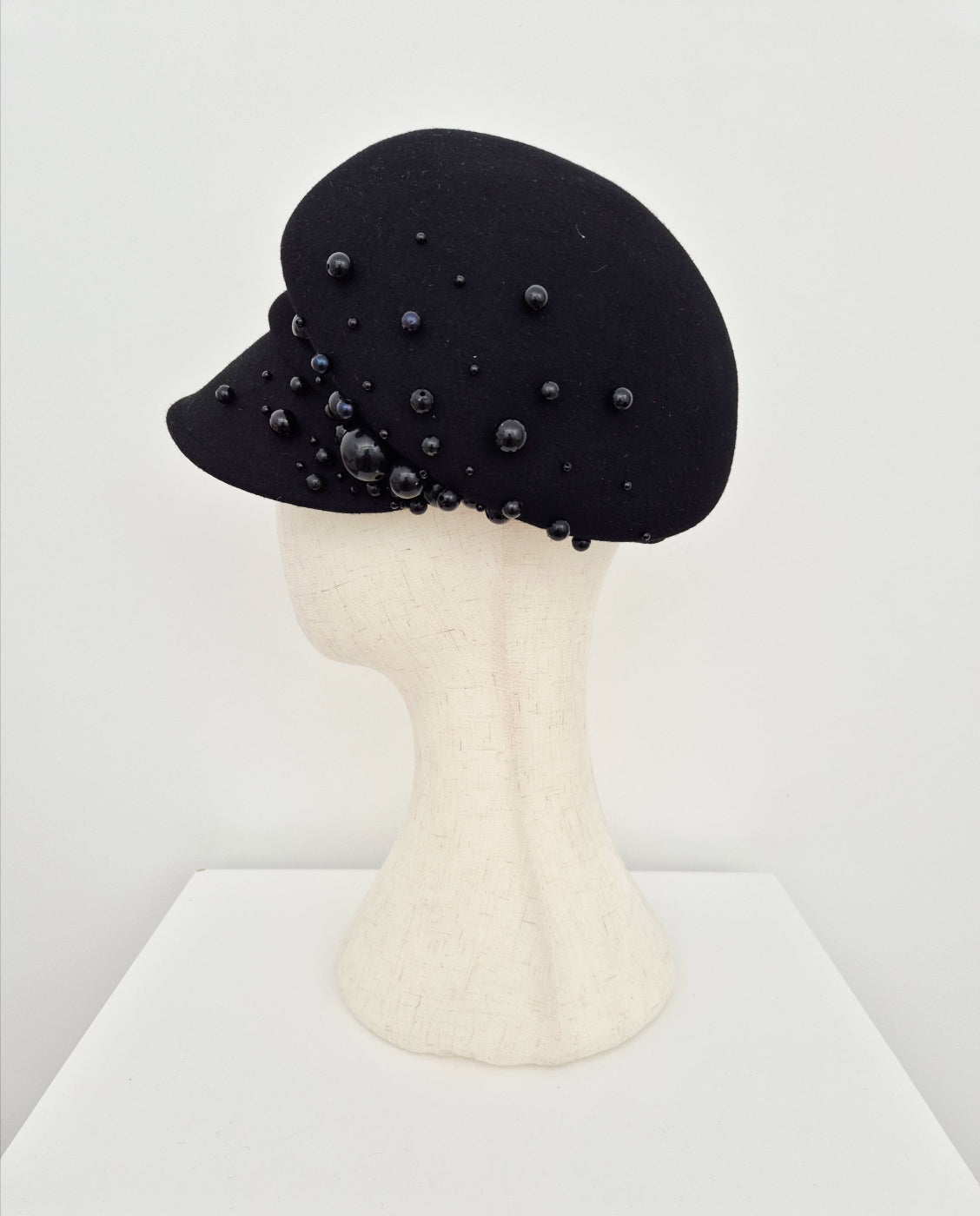 Black hat with bead embellishments on a mannequin head against a white background