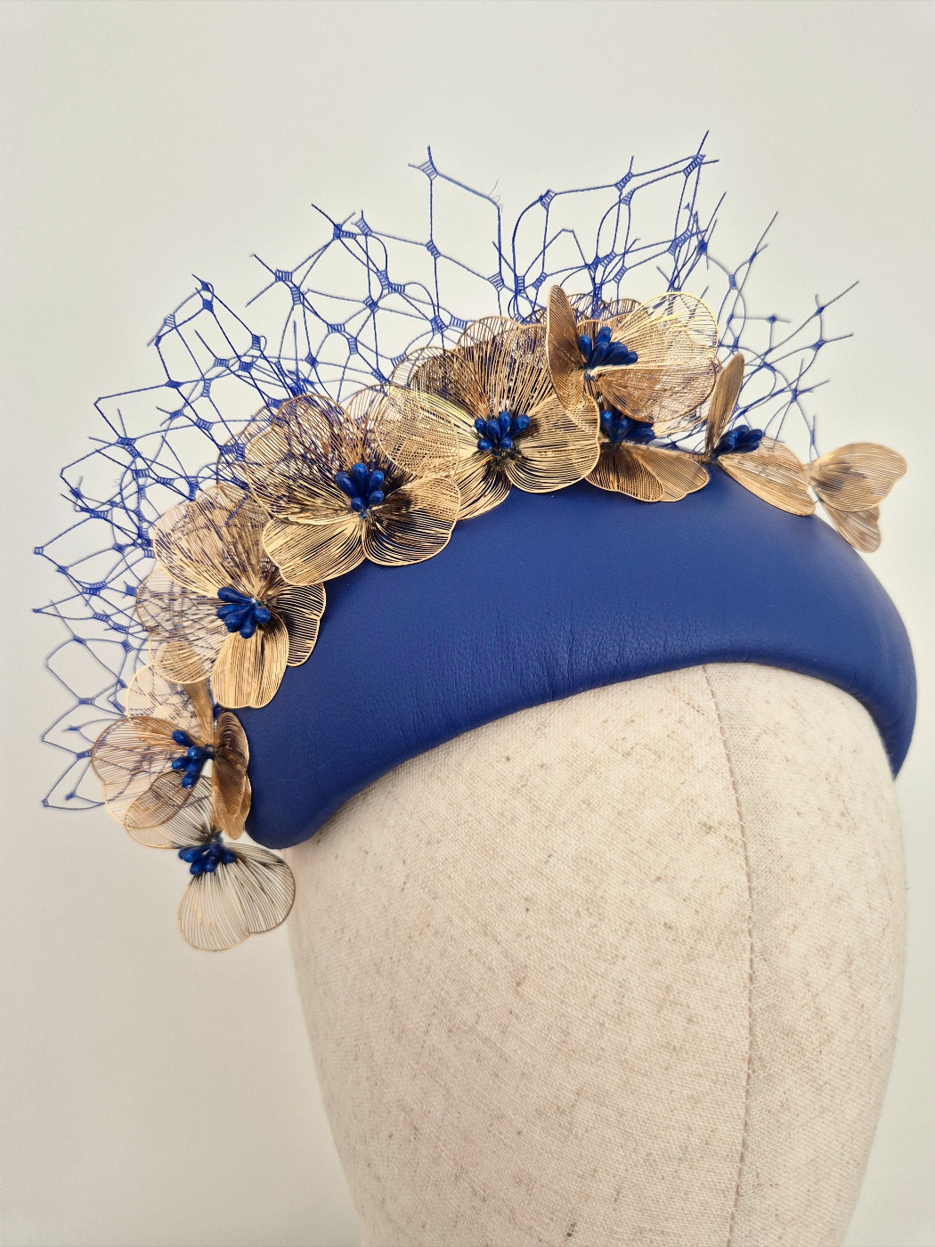 Blue headpiece with gold floral embellishments on a mannequin head against a light gray background close up