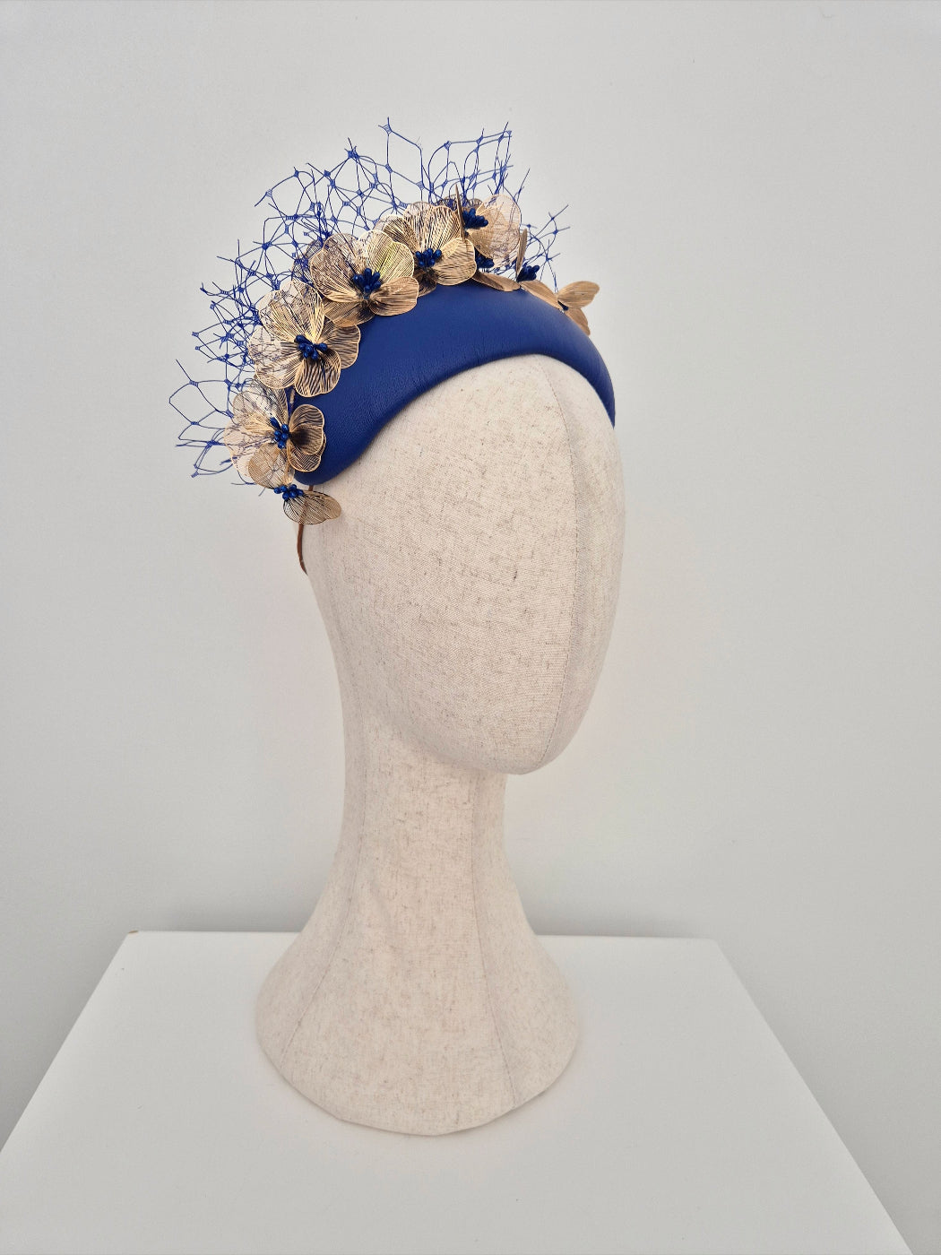 Blue headband with floral decorations on a mannequin head against a gray background side view