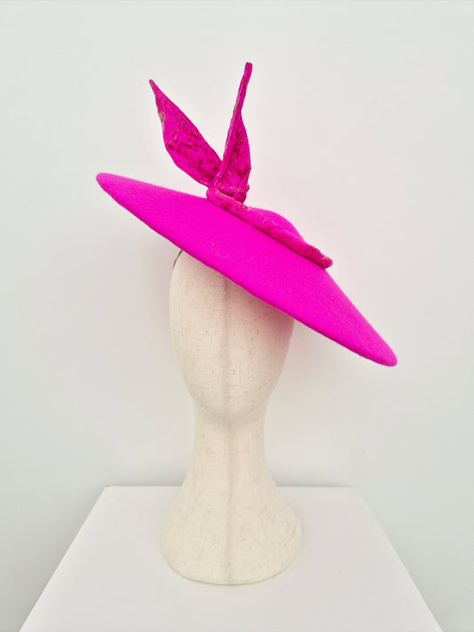 Bright pink wide-brimmed hat with decorative elements on a mannequin head against a white background