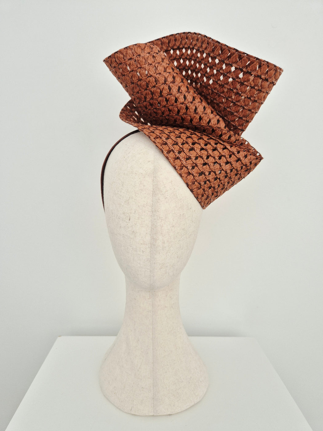 Brown straw headpiece on a mannequin head against a white background