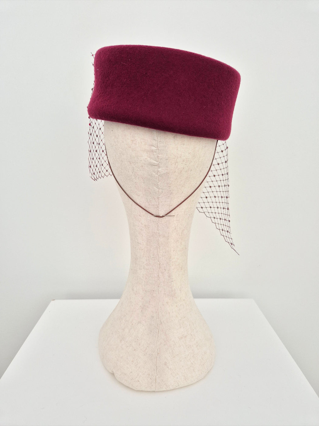 Mannequin head wearing a burgundy hat with a veil on a white background back view