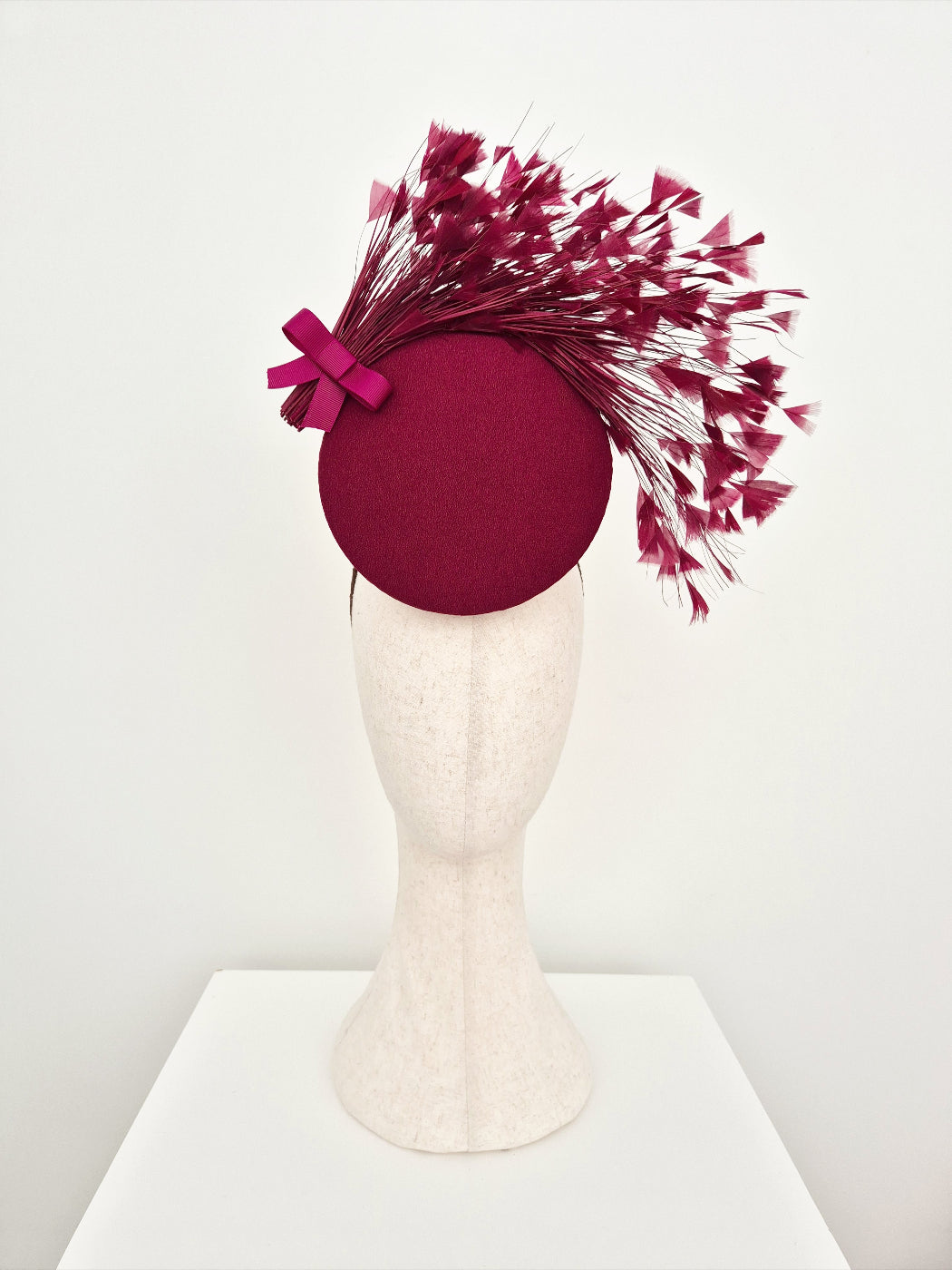 burgundy percher headpiece with feather accents on a mannequin head against a white background