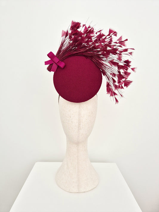burgundy percher headpiece with feather accents on a mannequin head against a white background
