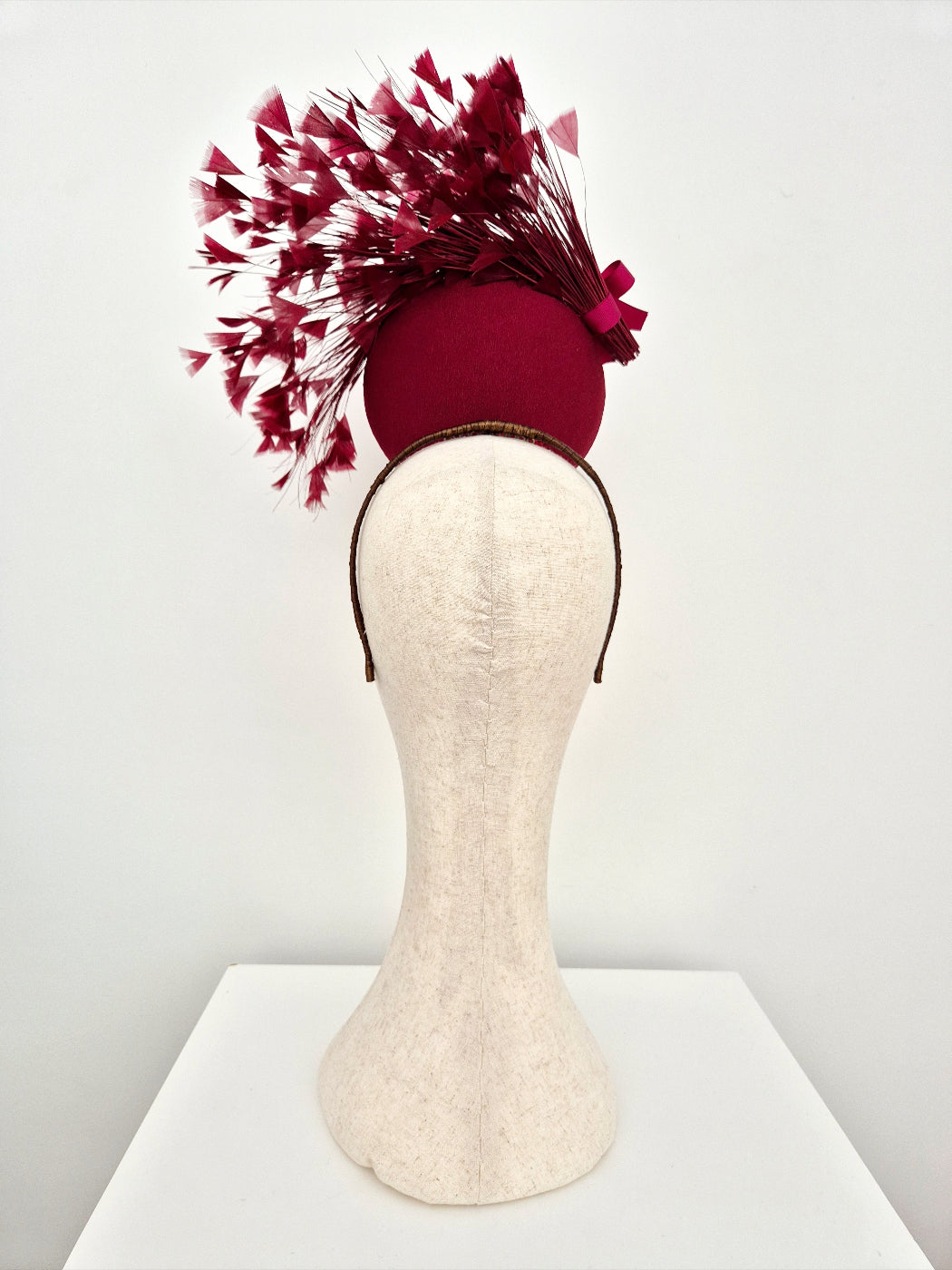 burgundy percher headpiece with feather accents on a mannequin head against a white background back view