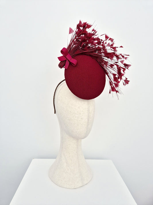 Burgundy percher  headpiece with feathers details on a mannequin head against a white background