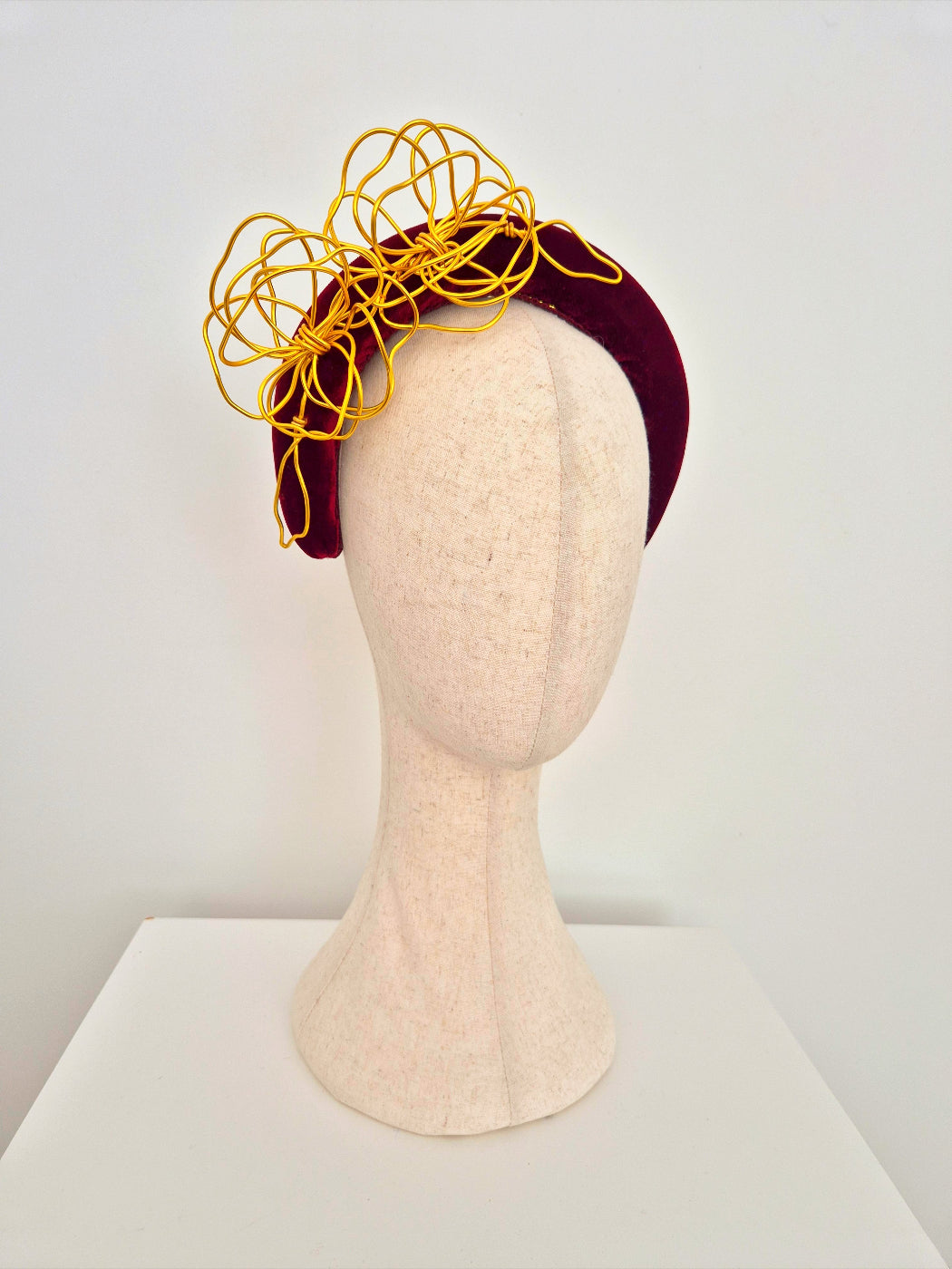 Mannequin head wearing a burgundy headband with gold wire flowers on a white background side front view