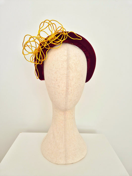 Mannequin head wearing a burgundy headband with gold flowers on a white background