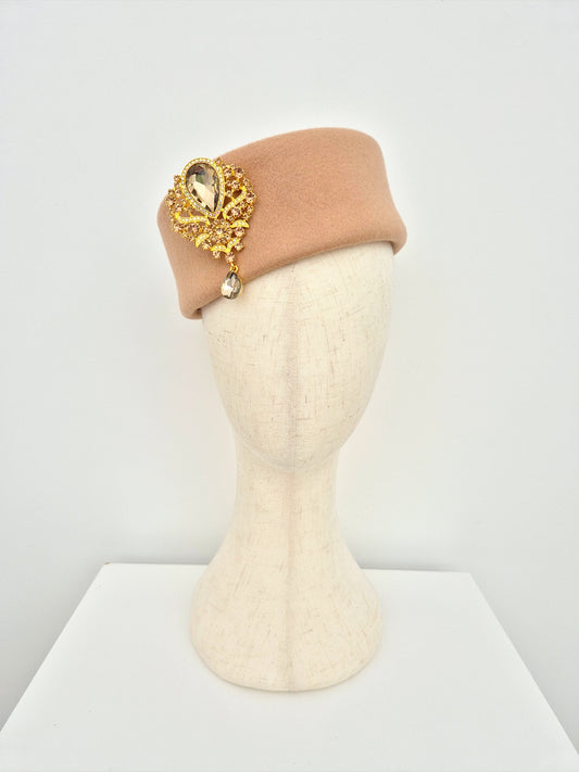 Beige pillbox headpiece with decorative gold element on a mannequin head against a white background