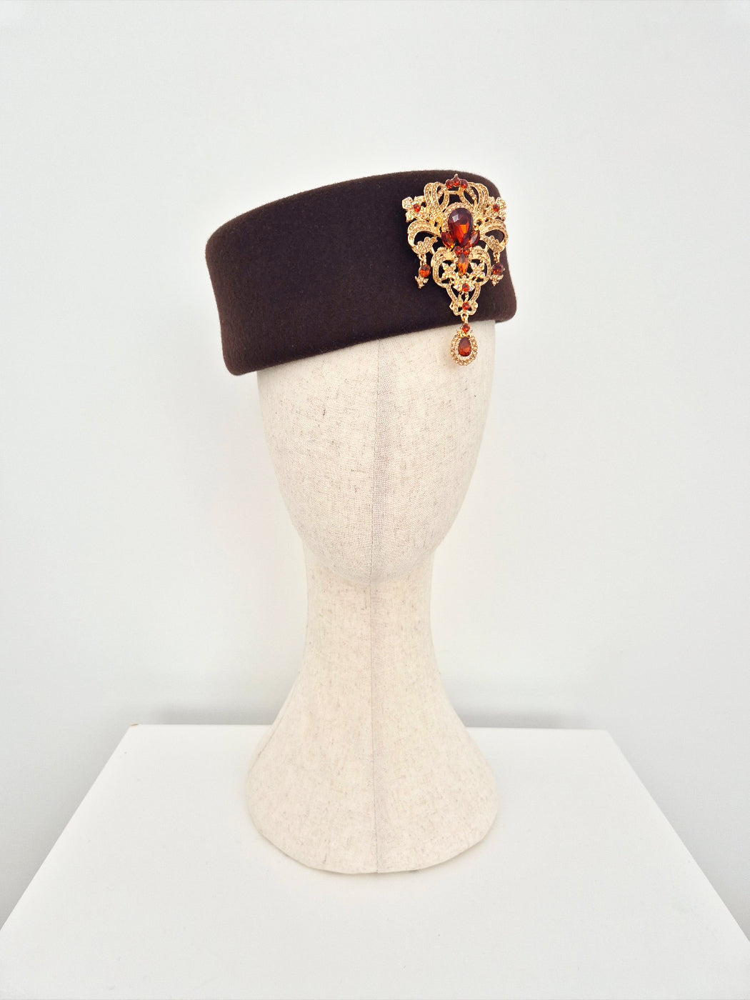 Brown hat with decorative emblem on a mannequin head against a white background