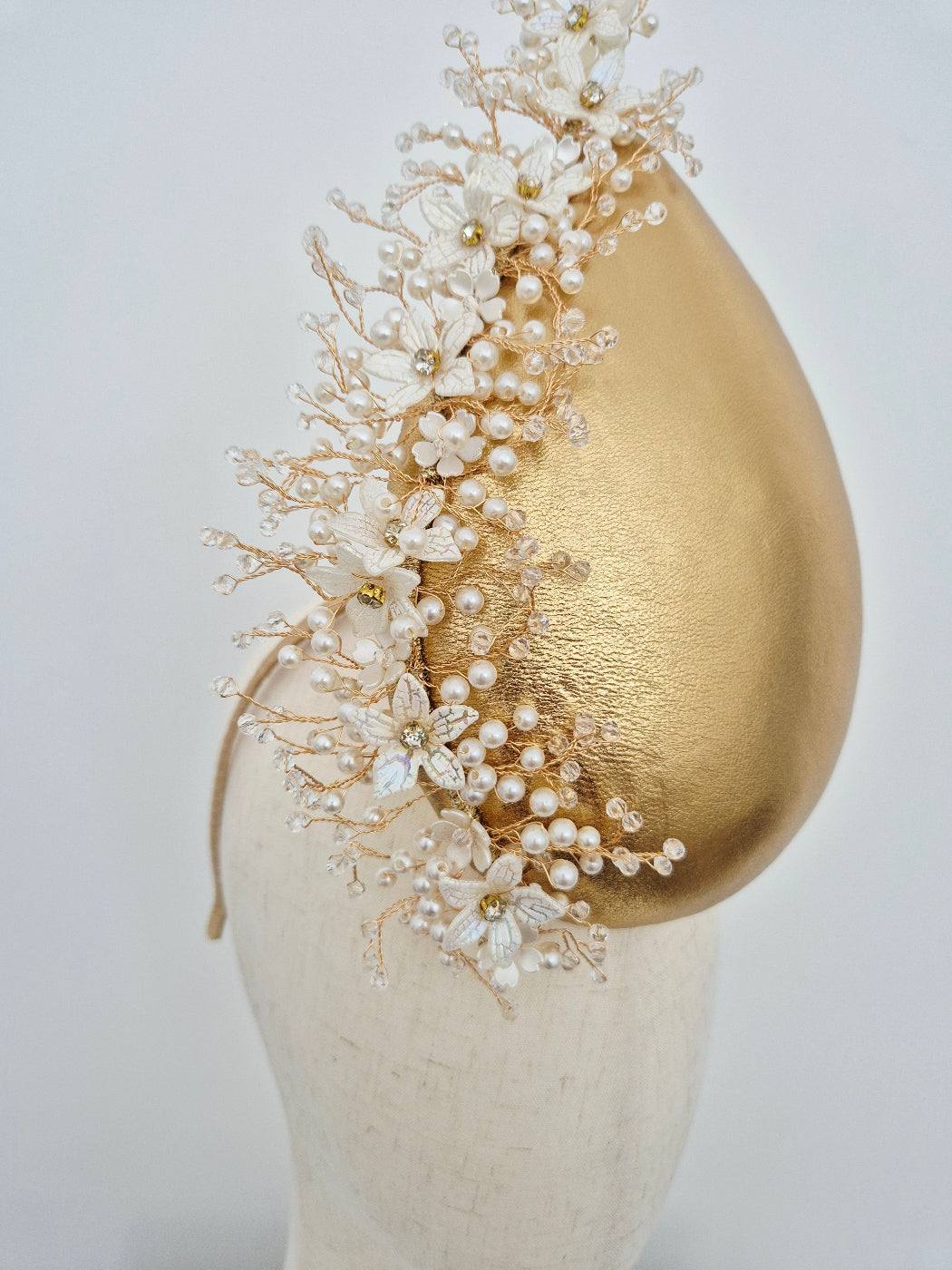 close up of Delicate pearl embellishment on a gold percher headpiece on a mannequin head against a white background